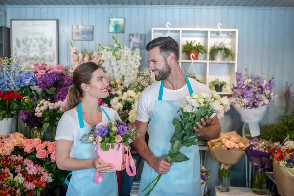 Varón barbudo y hembra de cabello castaño en delantales sosteniendo flores, mirándose unos a otros —  Fotos de Stock