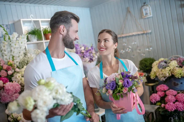 Varón barbudo y hembra de cabello castaño sosteniendo flores, mirándose, sonriendo —  Fotos de Stock