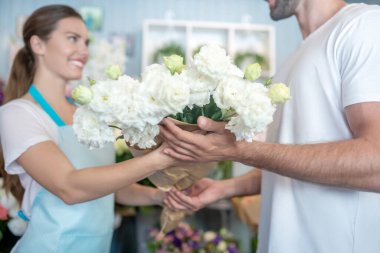 Gülümseyen kadın çiçekçi erkeğe bir buket beyaz çiçek veriyor.