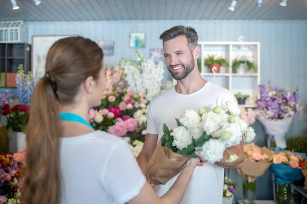 Smiling male taking bouquet of white flowers from female florist — Stock Photo, Image