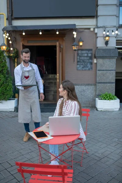 Camarero barbudo trayendo una copa de vino tinto al cliente femenino — Foto de Stock