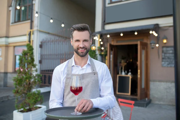 Бородатый официант держит поднос с бокалом красного вина — стоковое фото