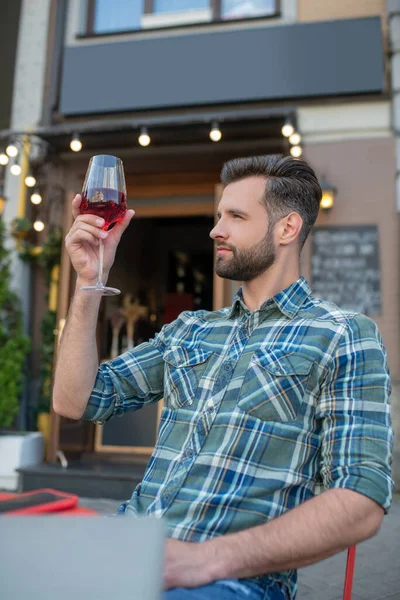 Sakallı erkek açık hava kafesinde oturmuş, bir bardak kırmızı şaraba bakıyor. — Stok fotoğraf