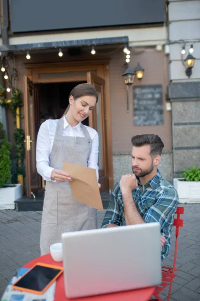 Smiling waitress showing menu to bearded male, pressing his fist to chin — Stock Photo, Image