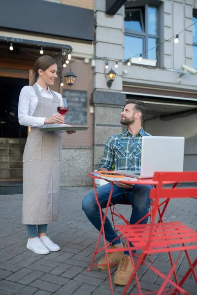 Camarera sonriente trayendo una copa de vino a un hombre barbudo — Foto de Stock