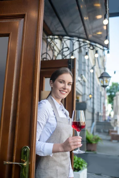 Le söt servitris i grått förkläde håller glas vin — Stockfoto