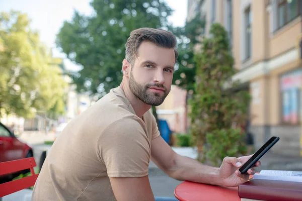 Maschio barbuto seduto nel caffè, tenendo smartphone, sorridente — Foto Stock