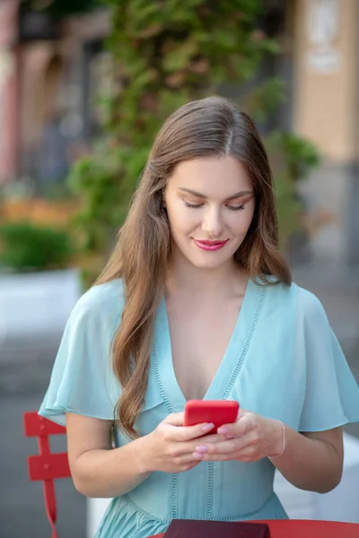 Kırmızı dudaklı romantik bir kadın açık hava kafesinde oturuyor, mesajlaşıyor, gülümsüyor. — Stok fotoğraf