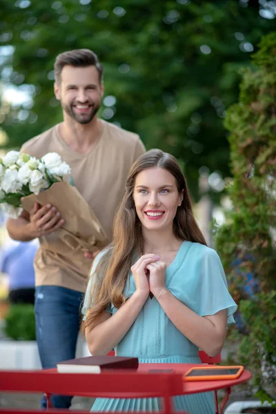 Jovem mulher sentada no café, barbudo macho chegando a ela com flores — Fotografia de Stock