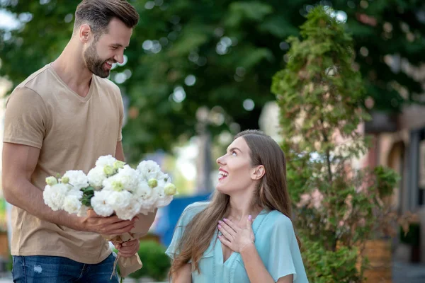 Bearded male presenting flowers to surprised cute female — Stock Photo, Image