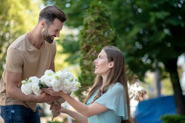Бородатий чоловік представляє букет з білих квітів красивій жінці — стокове фото