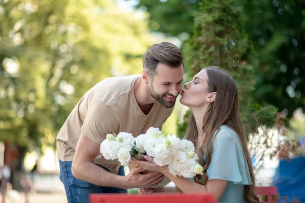 Bearded male presenting flowers to pretty female, kissing him on cheek