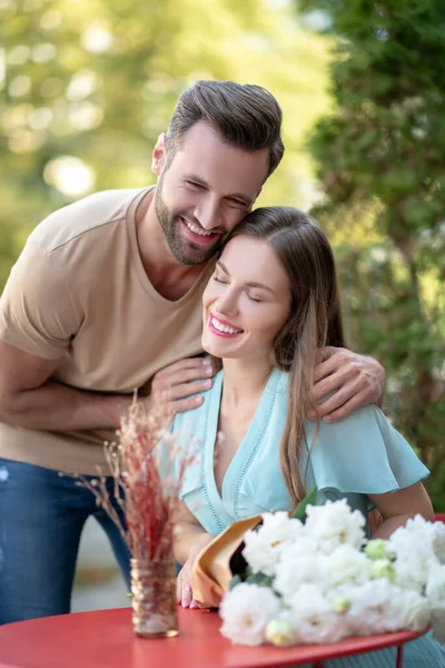 Bärtiger Mann umarmt lächelnde Frau, zeigt seine Zuneigung, beide lächeln — Stockfoto