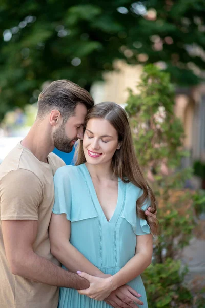 Bärtiger Mann umarmt zärtliche Frau in blauem Kleid und drückt seine Stirn vor ihr Gesicht — Stockfoto