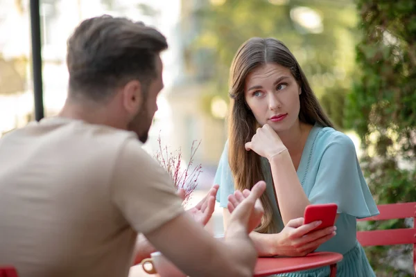 Couple having misunderstanding in open air cafe, sad female holding her phone — Stock Photo, Image