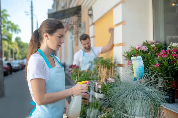 Jonge mooie vrouwelijke spuiten planten buiten bloemenwinkel, bebaarde vrouw staan achter — Stockfoto