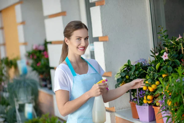 若い笑顔の女性は花の店の外の植物を噴霧 — ストック写真