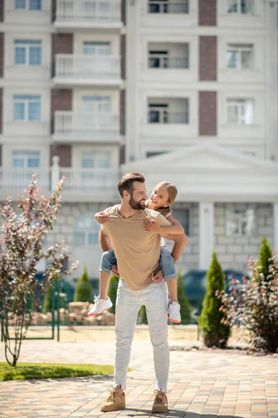 Baba kızını sırtında tutuyor ve gülümsüyor.