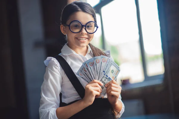 Flicka i vit skjorta håller dollar och ser nöjd ut — Stockfoto