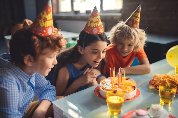 Tři děti se dívají na dort a jsou vzrušené — Stock fotografie