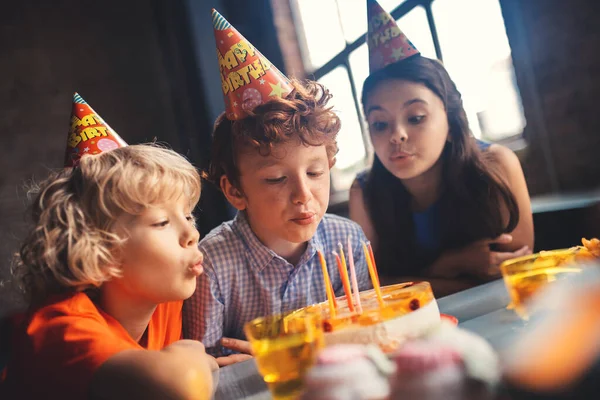 Tres niños sentados en la mesa y soplando los cañones — Foto de Stock