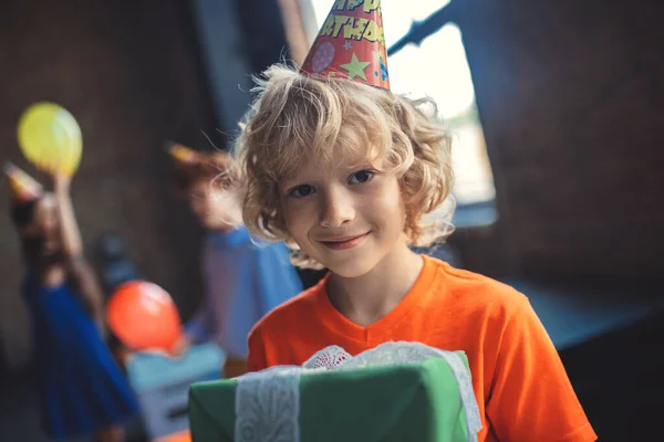 Leuke blonde jongen met een geschenk en glimlach — Stockfoto