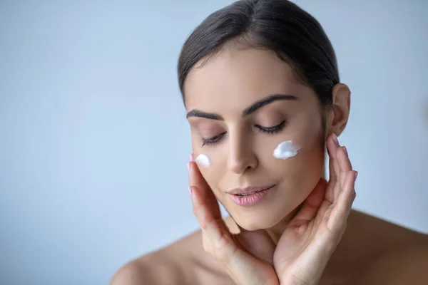 Mujer linda con crema en sus mejillas buscando relajado —  Fotos de Stock