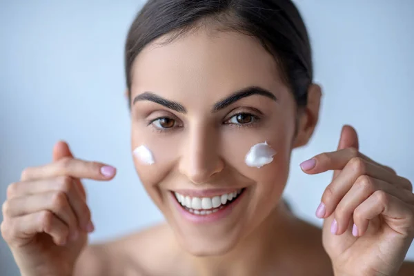 Cute woman with cream on her cheeks looking cheerful — Stock Photo, Image