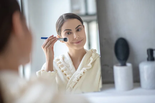 Leuke vrouw zit aan de spiegel en houdt een borstel vast — Stockfoto