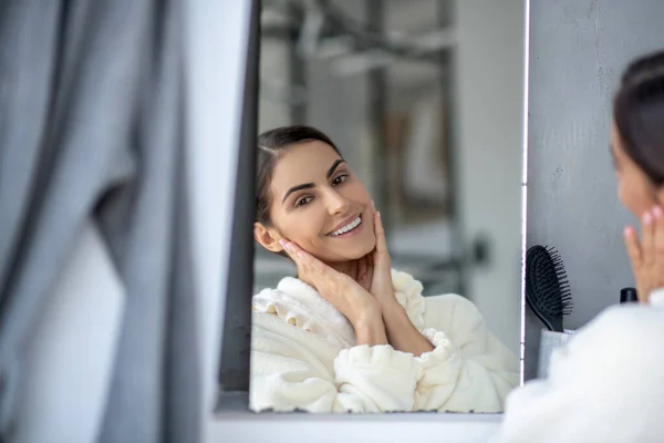 Милая женщина сидит перед зеркалом и чувствует себя счастливой — стоковое фото