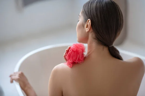 Mujer sosteniendo una esponja roja y sentada en el baño — Foto de Stock