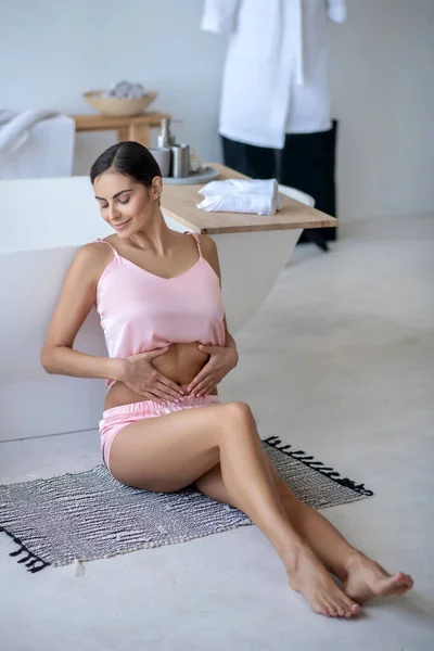 Mujer en lencería rosa tocando su abdomen y sonriendo — Foto de Stock