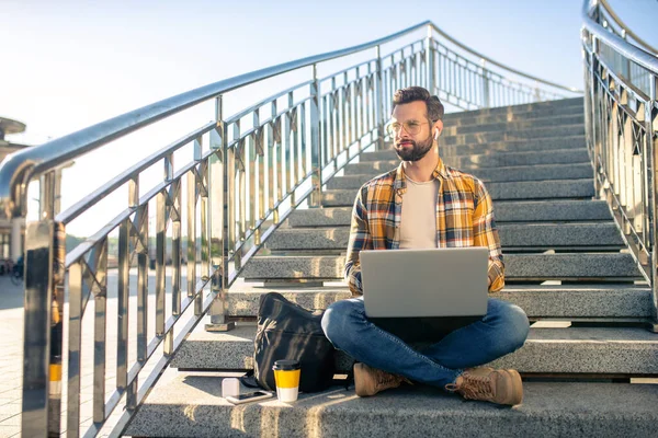 Bearded man with laptop on stairs outdoors