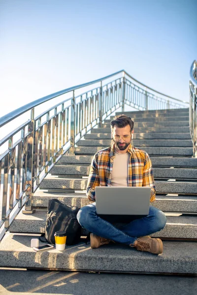 Ung man i glasögon med laptop på trappor utomhus — Stockfoto