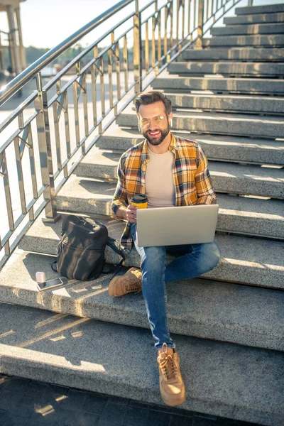 Zufriedener Mann mit Kaffee und Laptop auf Stufen — Stockfoto