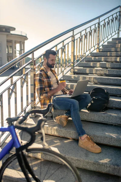 Uomo con laptop e caffè seduto sulle scale vicino alla bici — Foto Stock