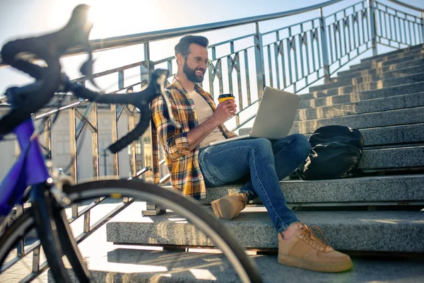 Uomo allegro con caffè e laptop sui gradini — Foto Stock