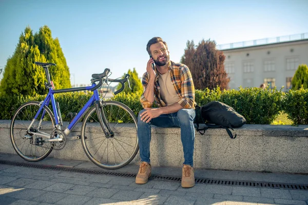 Радостный мужчина, сидящий на улице и разговаривающий по смартфону — стоковое фото