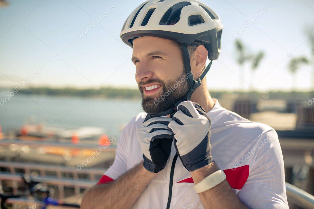 Concentrated man in sports gloves buttoning helmet