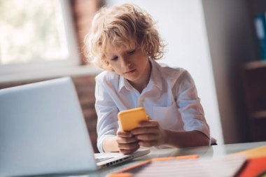 Akıllı telefonunu tutan ve mesajlaşan tatlı sarışın çocuk.