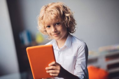 Güzel sarışın çocuk tabletini tutuyor ve gülümsüyor.