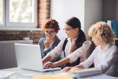 Koyu saçlı kız sınıf arkadaşlarına malzeme anlatıyor.