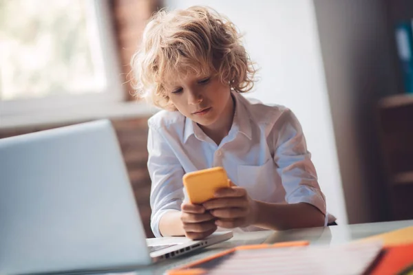 Netter blonder Junge hält sein Smartphone und SMS — Stockfoto