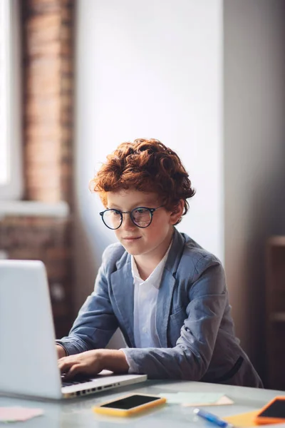 Rudovlasý chlapec sedí u laptopu a píše — Stock fotografie