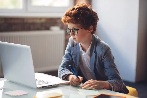 Roodharige jongen in zitten aan de laptop en kijken serieus — Stockfoto