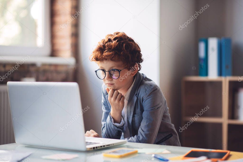 Red-haired boy in sitting at the laptop and looking busy