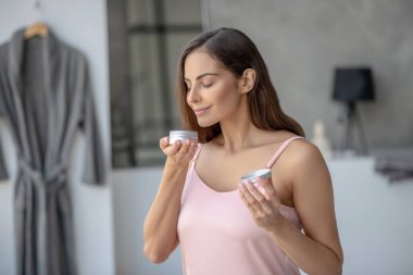 Güzel bir kadın bir kavanoz krem tutuyor ve onu kokluyor.