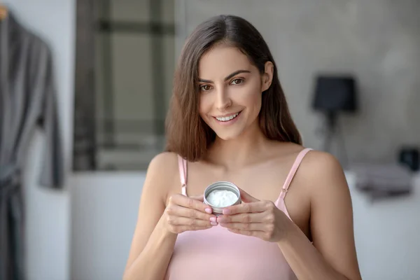 Hermosa mujer un frasco de crema para la piel y buscando complacido — Foto de Stock