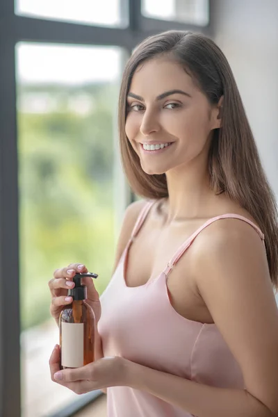 Hermosa mujer sosteniendo una botella de loción corporal y sonriendo — Foto de Stock