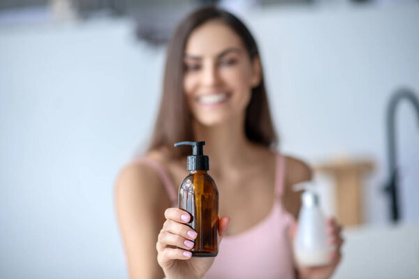 Pretty long-haired woman holding beauty products and smiling
